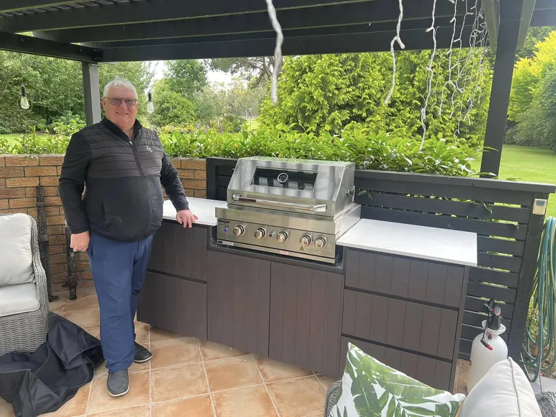 Outdoor kitchen cabinetry built by D.J. Morrison under a pergola with a stone benchtop