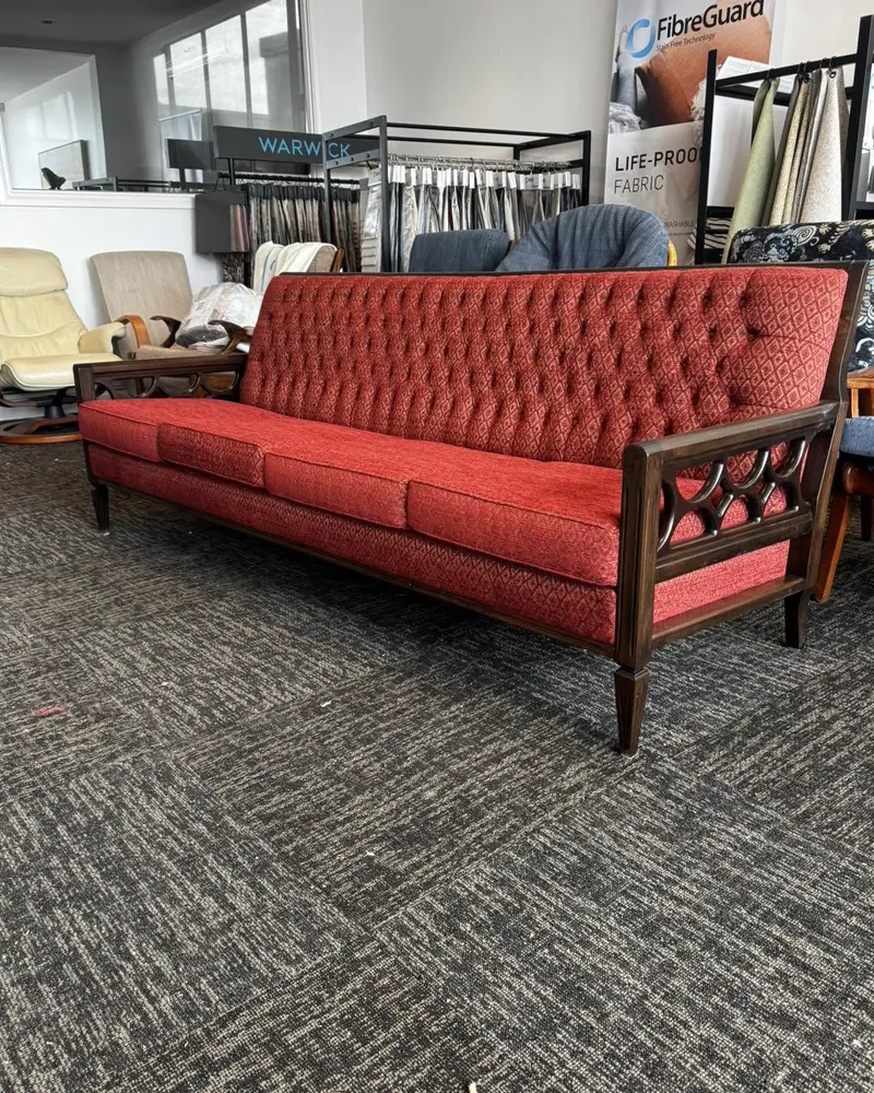 The matching sofa after restoration, buttoned red upholstery with a polished timber frame